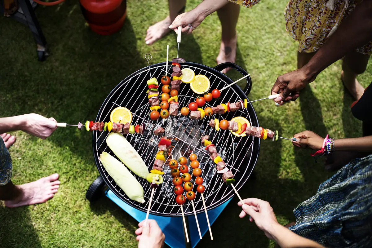 Vue aérienne de brochettes de viande et légumes grillant sur un barbecue au charbon lors d'un repas d'été entre amis